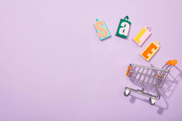 Draufsicht auf bunte Einkaufstüten mit Verkaufsaufschrift, die in einen Spielzeugwagen auf violett fallen — Stockfoto