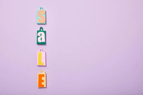 Flat lay with colorful shopping bags with sale lettering on violet — Stock Photo