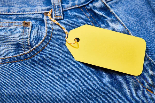 Close up view of yellow paper sale tag on rope on jeans — Stock Photo