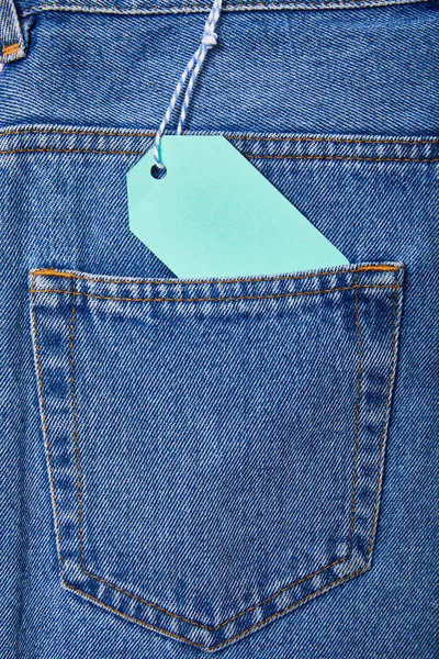 Close up view of turquoise paper sale tag on rope on jeans — Stock Photo
