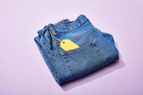 Jeans con etiqueta de venta de papel amarillo en cuerda sobre fondo violeta - foto de stock