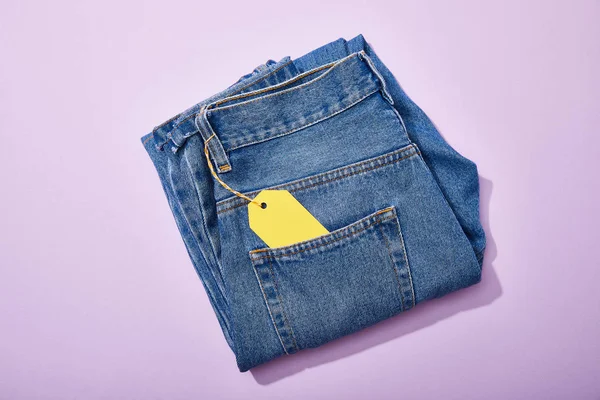 Vista superior de jeans con etiqueta de venta de papel amarillo en cuerda sobre fondo violeta - foto de stock