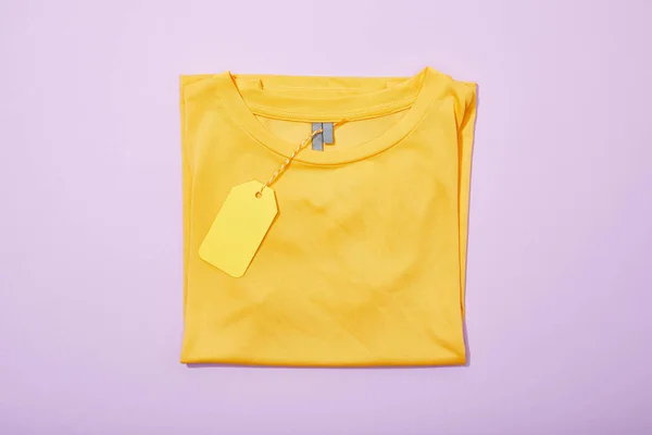 Top view of yellow sale tag on rope on t-shirt on violet — Stock Photo