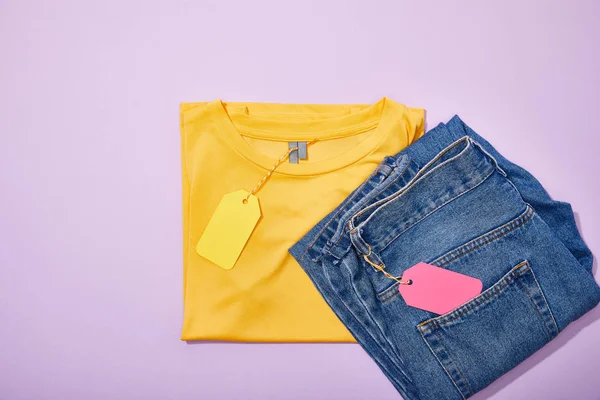 Vue du haut des étiquettes de vente colorées sur t-shirt et jeans sur violet — Photo de stock