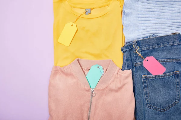 Flat lay with colorful clothes with paper sale tags on ropes on violet — Stock Photo