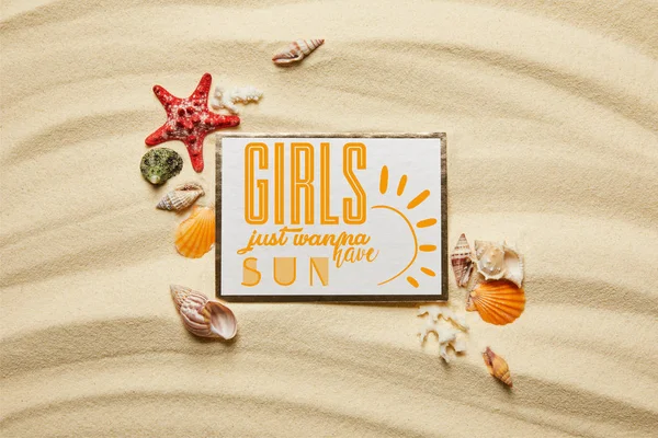 Top view of placard with girls just wanna have sun lettering near seashells, starfish and white corals on sandy beach — Stock Photo