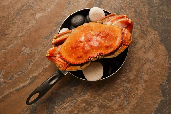 Vue de dessus du crabe non cuit avec coquille solide avec des pierres noires dans une poêle sur surface texturée — Photo de stock