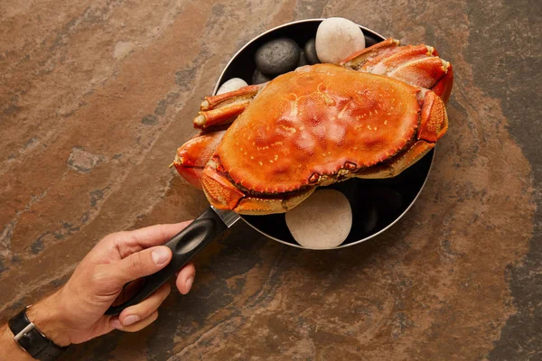 Cropped view of uncooked crab with solid shell with black stones in frying pan on textured surface — Stock Photo