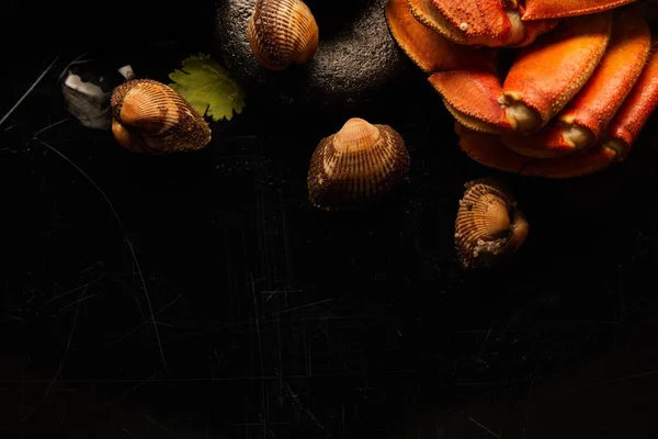 Vista de cerca de cangrejo crudo, berberechos y mejillones con vegetación sobre piedras aisladas en negro - foto de stock