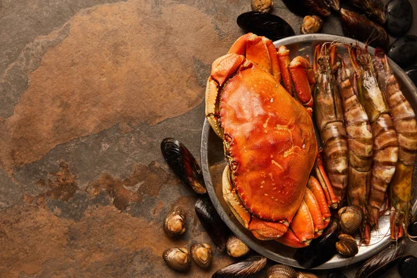 Vista superior de cangrejo, mariscos, berberechos y mejillones sin cocer en un tazón sobre una superficie texturizada - foto de stock