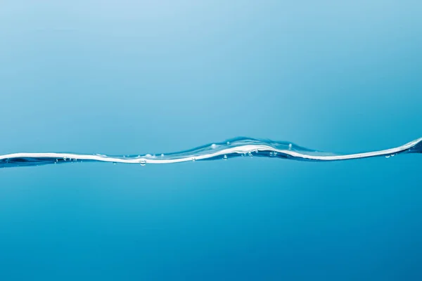 Vague d'eau pure transparente avec des gouttelettes sur fond bleu — Photo de stock