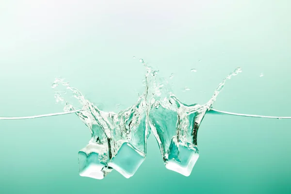 Transparent pure water with splash and ice cubes on green background — Stock Photo