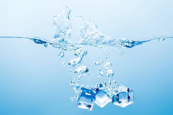 Água pura com respingo, bolhas e cubos de gelo no fundo azul — Fotografia de Stock