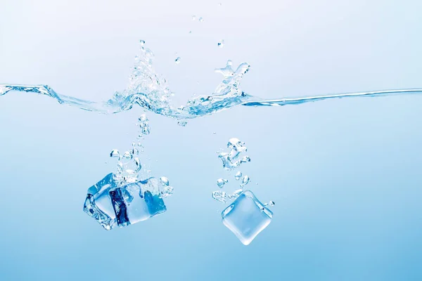 Agua pura transparente con salpicaduras y cubitos de hielo sobre fondo azul — Stock Photo
