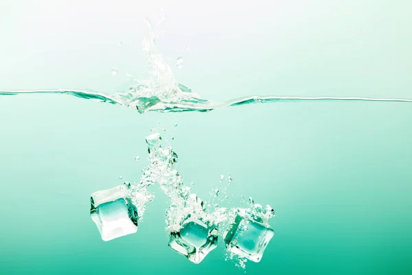 Transparent pure water with splash, ice cubes and bubbles on green background — Stock Photo