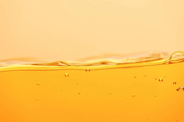 Liquide brillant jaune ondulé avec éclaboussures et bulles isolées sur jaune — Photo de stock