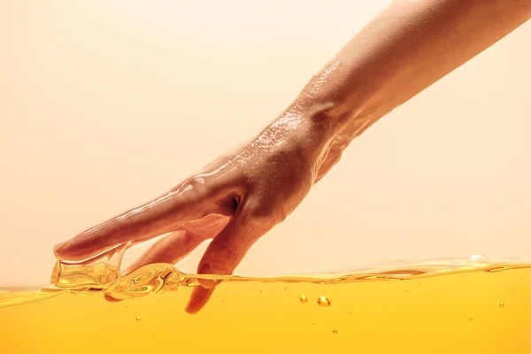 Partial view of hand touching yellow bright liquid isolated on yellow — Stock Photo