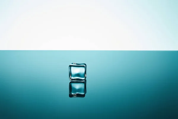 Cubo de hielo transparente con reflexión sobre el fondo esmeralda y blanco - foto de stock