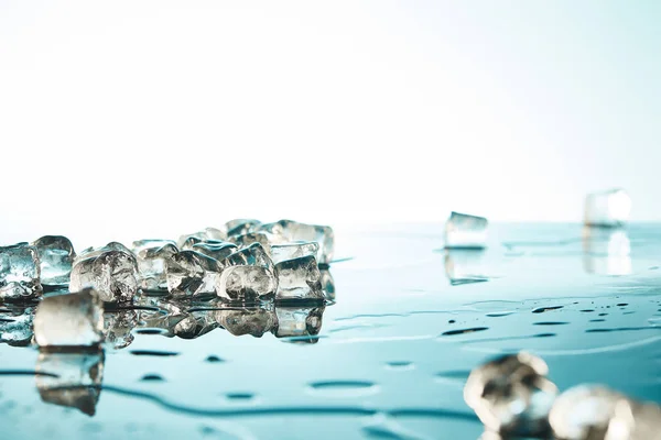 Montón de cubitos de hielo fundido transparente con charcos de agua sobre fondo esmeralda y blanco - foto de stock