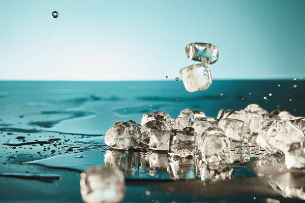 Cubos de hielo de fusión transparentes con charcos sobre fondo esmeralda y blanco - foto de stock