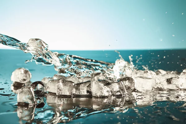 Cubos de gelo de fusão transparentes com água salpicante sobre fundo esmeralda e branco — Fotografia de Stock