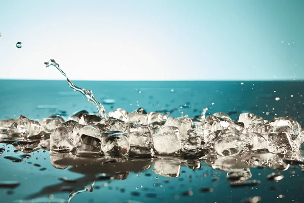 Derretendo cubos de gelo e respingo de água sobre fundo esmeralda e branco — Fotografia de Stock