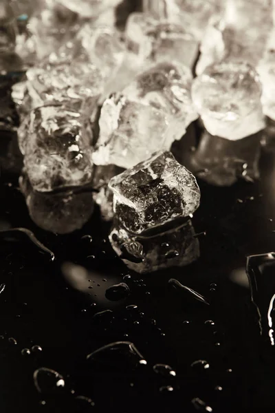 Стопка прозрачных холодных кубиков льда на черном фоне с каплями — стоковое фото