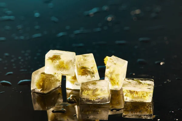Pila di cubetti di ghiaccio trasparente con fiori congelati su sfondo smeraldo — Foto stock
