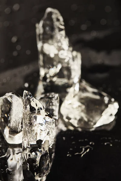 Cubos de hielo de fusión transparentes con gotas en la superficie negra - foto de stock