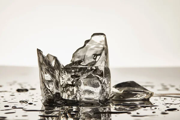 Cubos de gelo de fusão transparentes com poças no fundo branco — Fotografia de Stock