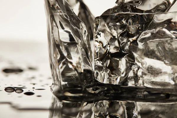 Vista de cerca de cubos de hielo de fusión transparentes con charcos sobre fondo blanco - foto de stock