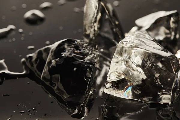 Vista de cerca de cubos de hielo de fusión transparentes con gotas sobre fondo negro - foto de stock