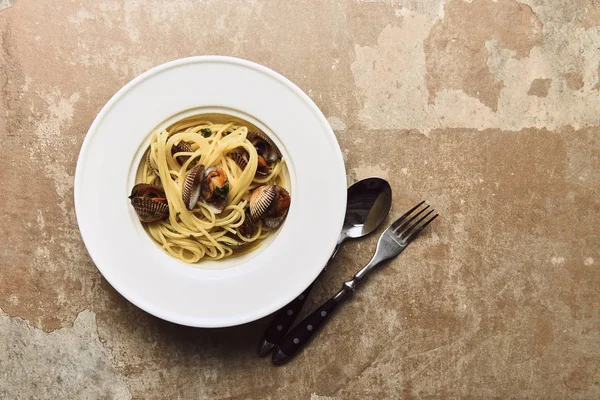 Vista dall'alto di deliziosa pasta con molluschi servita con cucchiaio e coltello su sfondo beige alterato — Foto stock