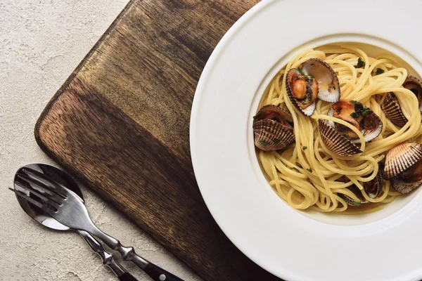 Vue rapprochée de délicieuses pâtes aux mollusques sur planche à découper en bois sur fond blanc — Photo de stock