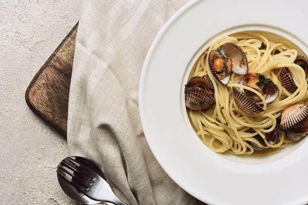 Верхний вид вкусной пасты с моллюсками на салфетке на деревянной доске резки на белом фоне — стоковое фото