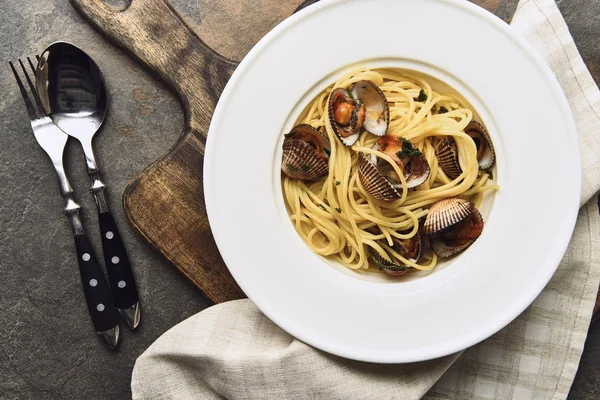 Top view of delicious pasta with mollusks on wooden cutting board near cutlery — Stock Photo