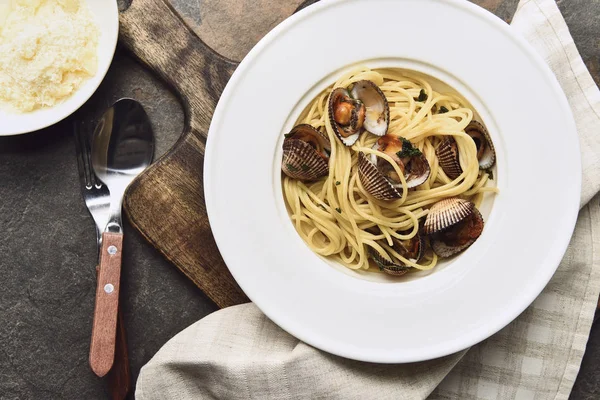 Vue du dessus de délicieuses pâtes aux mollusques sur une planche en bois avec serviette près du fromage râpé — Photo de stock