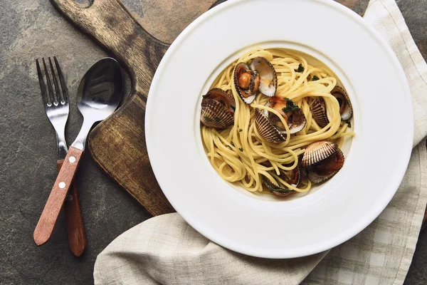 Верхний вид вкусной пасты с моллюсками на деревянной разделочной доске возле столовых приборов — стоковое фото