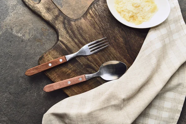 Top view of delicious grated Parmesan with napkin and cutlery on wooden cutting board — Stock Photo