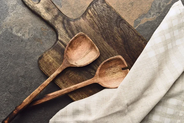 Top view of wooden cutting board with spatulas and napkin on weathered background — Stock Photo