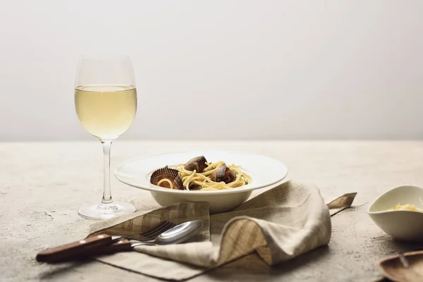 Pastas italianas con mariscos servidos con vino blanco, servilleta y cubiertos aislados en gris - foto de stock