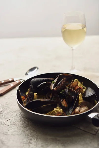 Foco seletivo de deliciosas massas italianas com frutos do mar servidos em frigideira com vinho branco isolado em cinza — Fotografia de Stock