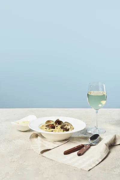 Deliziosi spaghetti italiani con frutti di mare serviti con vino bianco su tovagliolo vicino a posate isolate su blu — Foto stock