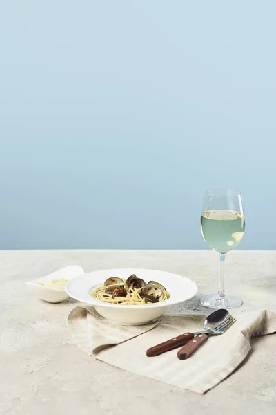 Delicious Italian spaghetti with seafood served with white wine on napkin near cutlery isolated on blue — Stock Photo