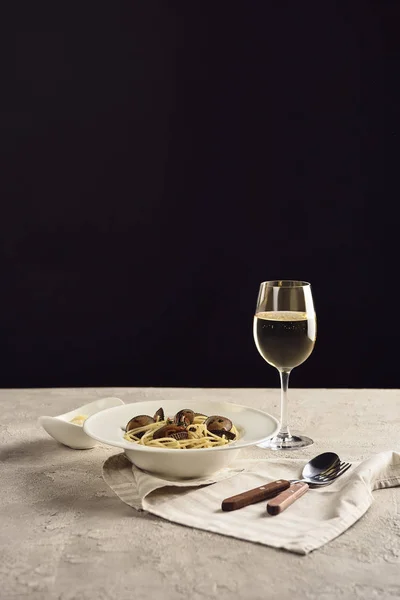 Deliciosos espaguetis italianos con mariscos servidos con vino blanco y queso rallado en servilleta cerca de cubiertos aislados en negro - foto de stock