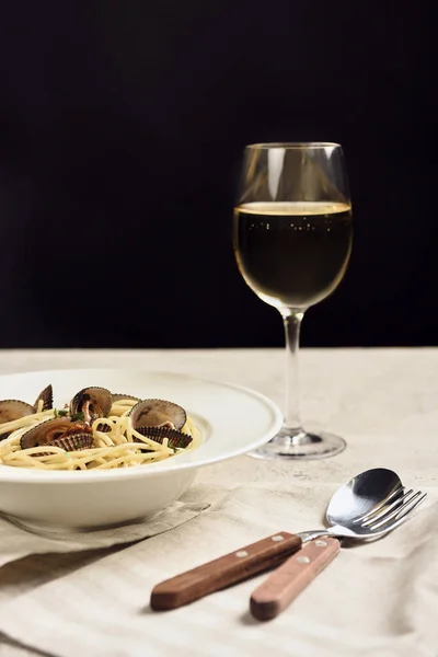 Deliciosos espaguetis italianos con mariscos servidos con vino blanco en servilleta cerca de cubiertos aislados en negro - foto de stock