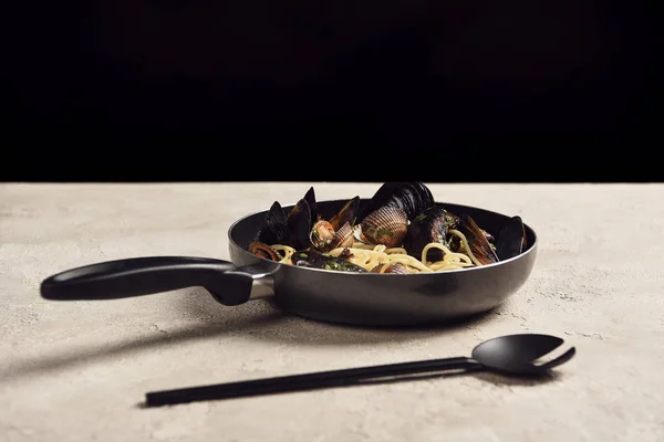 Delicious Italian pasta with seafood served in frying pan near spatula isolated on black — Stock Photo