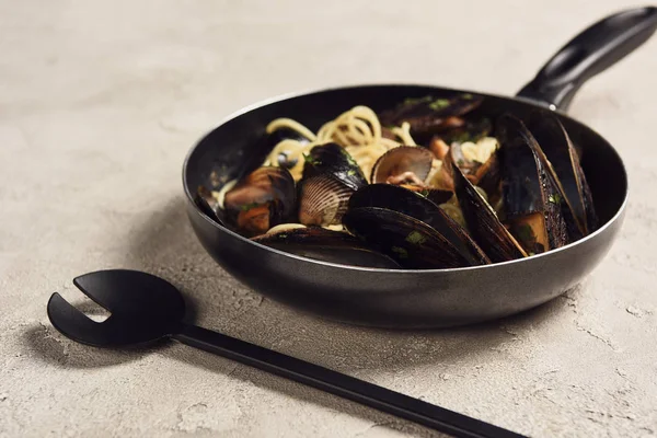 Delicious Italian pasta with seafood served in frying pan near spatula — Stock Photo