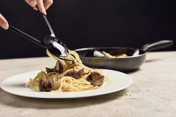 Abgeschnittene Ansicht einer Frau, die leckere italienische Spaghetti mit Meeresfrüchten auf Teller legt, isoliert auf schwarz — Stockfoto