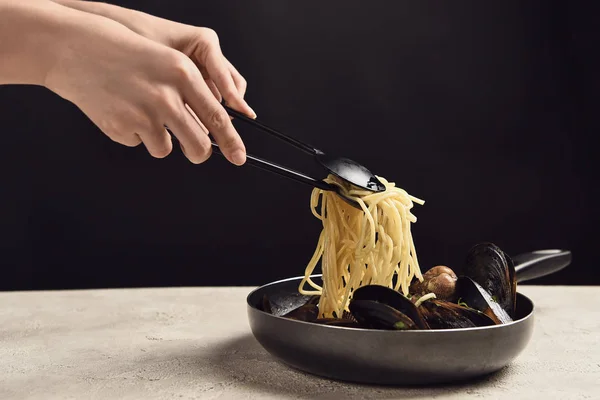 Cropped view of woman taking tasty Italian spaghetti with seafood from frying pan isolated on black — Stock Photo